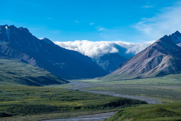 Denali National Park from Polychrome Pass on a sunny day, storm clouds roll across one mountain peak. Braided river in foreground