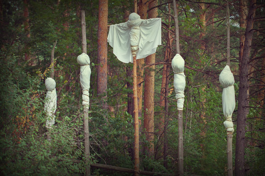 Sacrifices in a place of worship in the woods. Presentation of the victim in white clothes hanging on the trunks of trees. Ghosts in white robes in the forest. Eerie customs of ancient peoples.