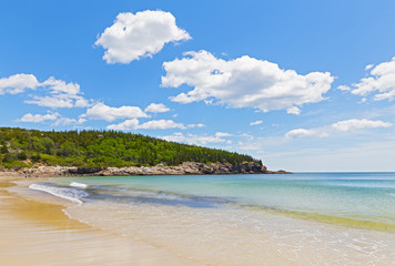 Ocean sandy beach in Acadia National Park, Maine, USA. Landscape with spruce forest and ocean waters under a blue sky with cumulus clouds.