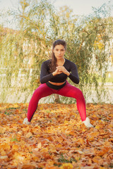 slim sporty woman squat in autumn city park