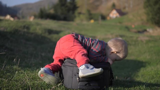 Amusing baby child try yo get up on big luggage in nature