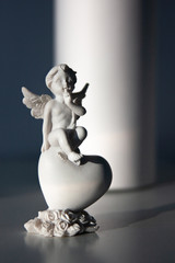 An angel statuette on the big heart on the table. Interior decoration