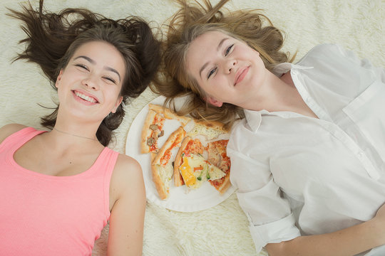 overeat happy girls lying on bed with pizza, laughing