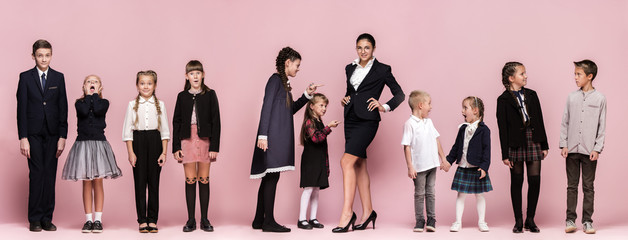 Cute smiling happy stylish children and female teacher on pink background. Beautiful stylish teen girls and boy standing together and posing at studio. Classic style. Kids fashion and emotions concept