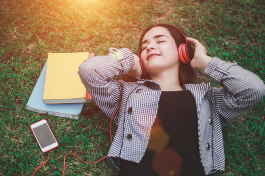 Education concept - Young woman are resting on the lawn in the college after studying the whole day by listening to music happy headphones.