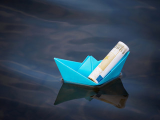 the ship is constructed of blue paper on Board which lies a twisted Euro banknote floating on the...