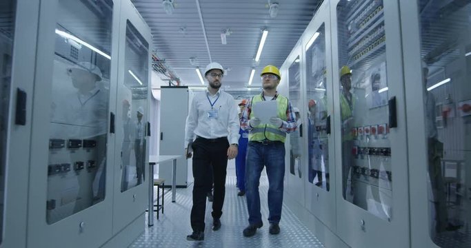 Wide shot of electrical workers walking and reviewing documents in the control room of an electrical station