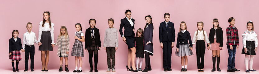 Cute smiling happy stylish children and female teacher on pink background. Beautiful stylish teen girls and boy standing together and posing at studio. Classic style. Kids fashion and emotions concept