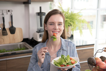 Healthy young woman eating salad in the kitchen