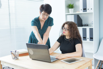 Business people, technology and communication concept - middle-aged woman showing something to another woman on laptop in office