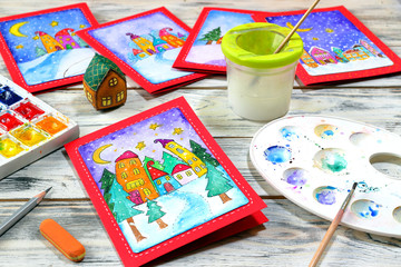 Winter watercolor greeting New Year (Christmas) cards with funny houses with watercolors and a brush for drawing on a white wooden background
