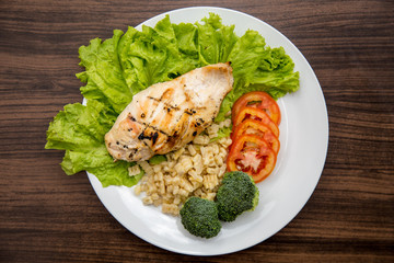 Healthy food salad bowl with tomatoes, chicken, broccoli, lime and mixed greens, lettuce in white plate on wooden background top view. Food and health.