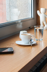 Cup of espresso, glass of water, smart phone, milk, on a window sill. Bussines coffee break concept.
