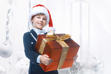 Beautiful little boy with a big Christmas gift in a Santa Claus hat. Christmas gifts for children. Smart boy Celebrates Christmas. New Year's holidays