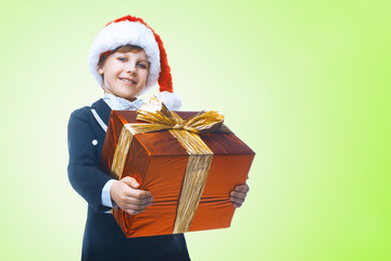 Beautiful little boy with a big Christmas gift in a Santa Claus hat. Christmas gifts for children. Smart boy Celebrates Christmas. New Year's holidays
