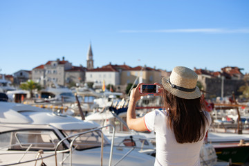 Young travelling woman in hat taking photos of summer sunny sea with smartphone camera. Brunette girl making photography on summer vacation