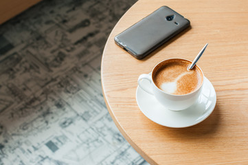 Cup of coffee and smartphone on a working table. Copy space, horizontal view.