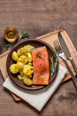 Salmon fish with baked potatoes on a plate on a cutting Board on a brown wooden background