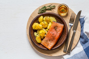 Fish salmon with baked potatoes on a plate on a round Board on a white Board
