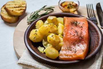 Fish salmon with baked potatoes on a plate on a round Board on a white Board