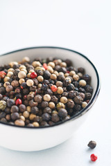 Various mixed pepper seeds in a white bowl on a white background. Macro photography.