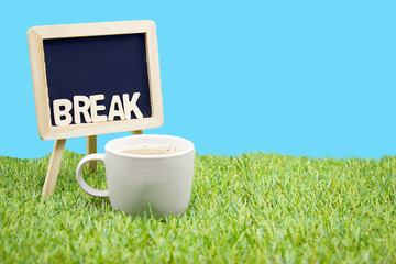 A cup of coffee is on green grass with isolated blue background