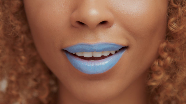 mixed race black blonde model with curly hair closeup of mouth painted with bright blue lipstick smile