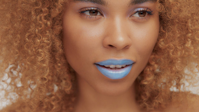 mixed race black blonde model with curly hair closeup of mouth painted with bright blue lipstick watching aside