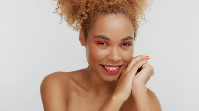 closeup portrait of mixed rase woman with red makeup in studio with hands on face smiling to the camera