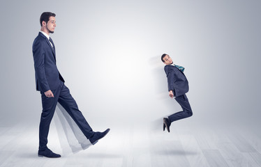 Big man in suit kicking out little himself with simple white wallpaper
