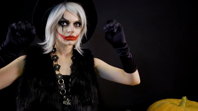 Scary beautiful girl witch celebrates halloween with funny glowing burning pumpkins in smoke. Female sorceress with gray hair scares, conjures, casts a spell