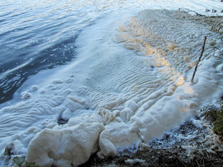 Dirty textured foam surface made by waves of water. Close-up view of abstract shore of a lake,...