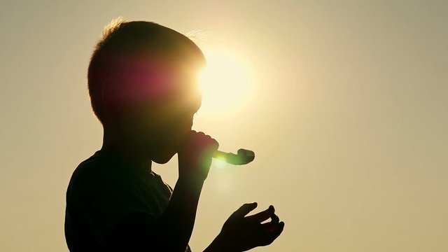 Silhouette of a happy child who blows a festive tongue-whistle. The boy plays with a whistle.