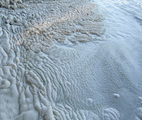 White wrinkled surface of foam made by water waves along a beach, close-up view. Beautiful pattern of natural texture.