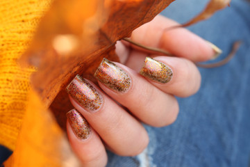 Female hands with natural nails in gold flakes hold a maple leaf