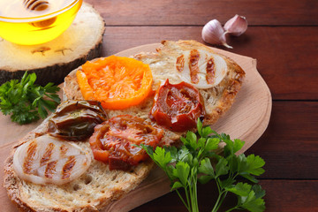 Toast with grilled vegetables. Vegetarian food. Red and yellow tomatoes. Grilled sandwich with tomatoes, onions and herbs. Bread with vegetables and honey. Vegan toast on wooden board