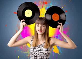 Young lady holding vinyl record on a grey background with colorful splashes behind her 