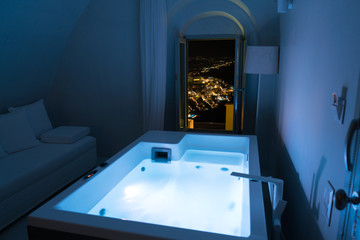 Luxury travel Santorini vacation hotel jacuzzi in colored lights with night view of the city. - obrazy, fototapety, plakaty