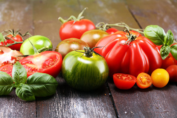 various colorful tomatoes and basil leaves on rustic table.