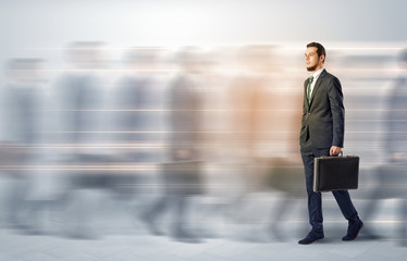 Young businessman with briefcase hurry up on a crowded street with blurred people around
