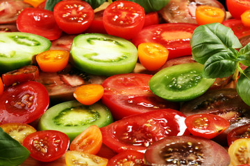 various colorful tomatoes and basil leaves on rustic table.