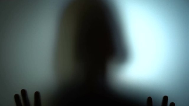 Silhouette of a deranged woman hammering on a glass, insane, lonely person. Blood-chilling horror thriller shot