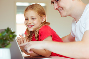 Happy young father have fun with his pretty daughter during working with laptop at home