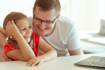 Happy young father have fun with his pretty daughter during working with laptop at home