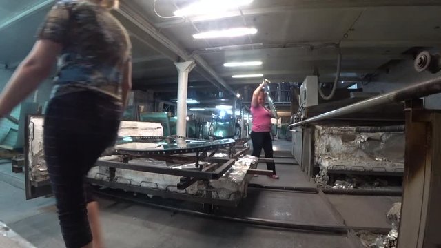 A woman takes out the glass from the bending oven. Production of autoglass.