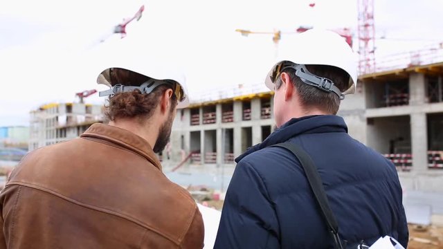 Two engineers talk about the project for the construction building. They look at both paper projects