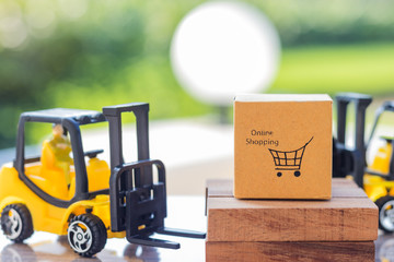 Cardboard box with shopping cart symbol on wooden block and mini forklift truck nearby with natural background. Logistics and transportation management ideas and Industry business commercial concept.