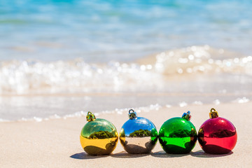 Obraz premium Four christmas multicolored decoration balls on seacoast with white sand and blue water on Phuket island, Thailand - travel X-mas and New Year holidays and vacation in tropics