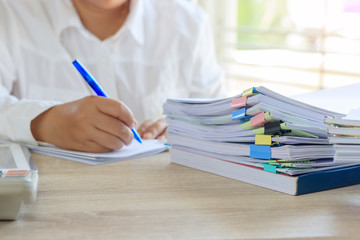 Teacher is checking student homework assignment and report on desk in school for score. Unfinished paperwork stacked in archive with color papers and paper clips. Education and business concept.