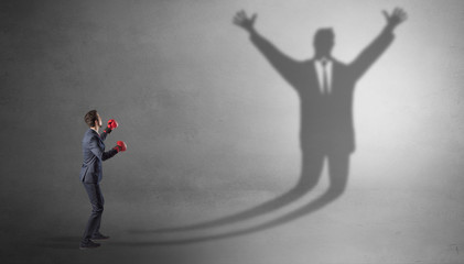 Businessman with boxing gloves fighting with disarmed businessman shadow
